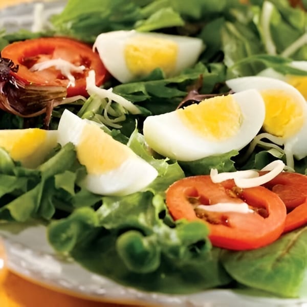 A fresh garden salad with hard-boiled egg wedges, sliced tomatoes, and mixed greens.