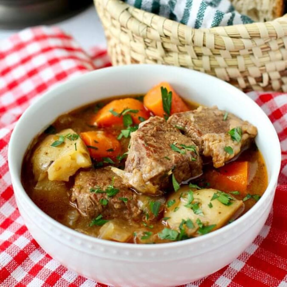Hearty British beef stew with carrots and potatoes in a white bowl on a red checkered cloth.
