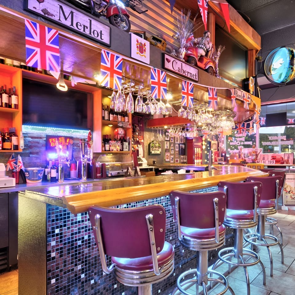 A British-themed bar with Union Jack flags, wine glasses, and purple bar stools.