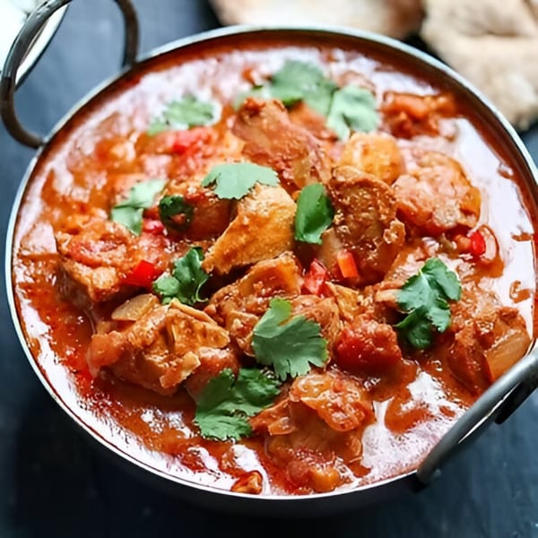 Close-up of a British chicken curry in a metal bowl, garnished with fresh cilantro.